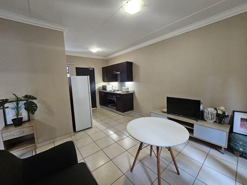 Open-plan living area featuring a compact kitchen with dark cabinetry, built-in oven and hob, and neutral tiled flooring throughout.