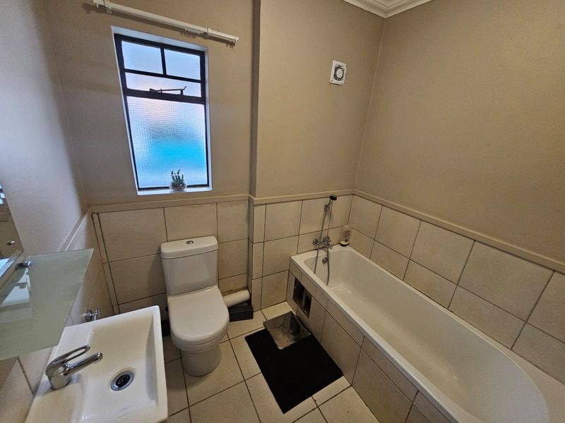A functional bathroom featuring a bathtub, toilet, and washbasin with tiled finishes and an extractor fan.