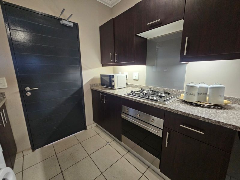A compact, functional kitchen featuring dark wood cabinetry, granite countertops, a gas hob, and a built-in oven with a modern glass splashback.