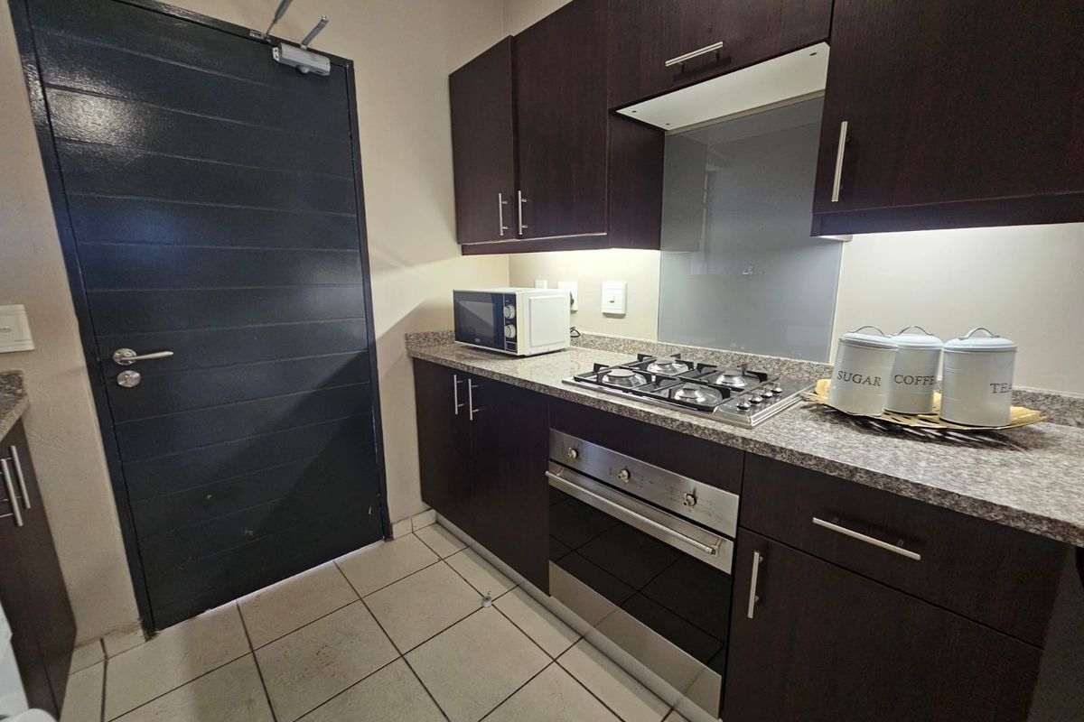 A compact, functional kitchen featuring dark wood cabinetry, granite countertops, a gas hob, and a built-in oven with a modern glass splashback.