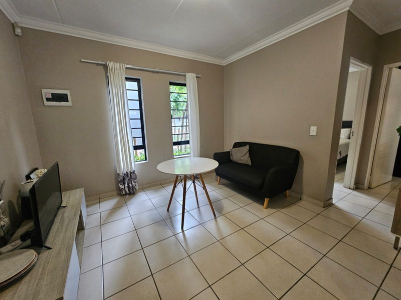 A functional living area featuring neutral wall tones, tiled flooring, and dual windows with aluminium frames, providing a bright and practical space.