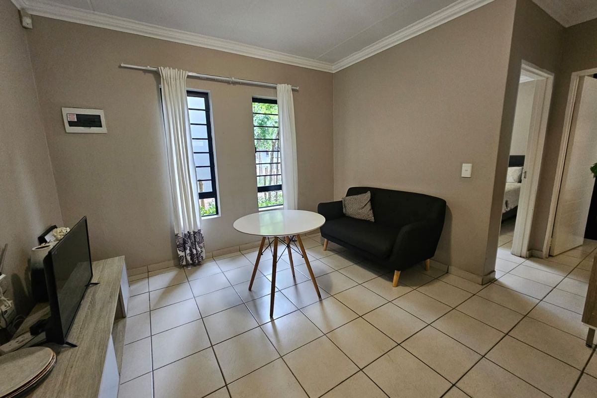 A functional living area featuring neutral wall tones, tiled flooring, and dual windows with aluminium frames, providing a bright and practical space.