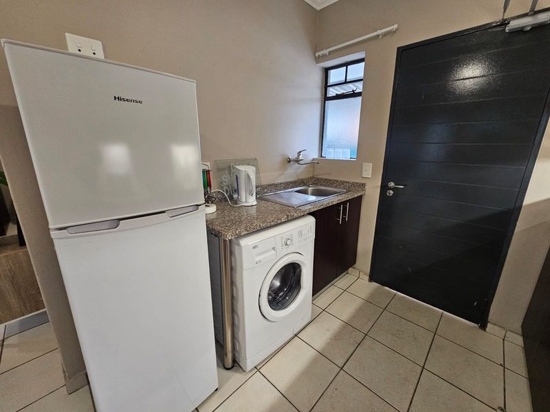 A functional laundry area featuring a granite countertop, stainless steel sink, built-in cabinetry, and tiled flooring with direct access to an exterior door.