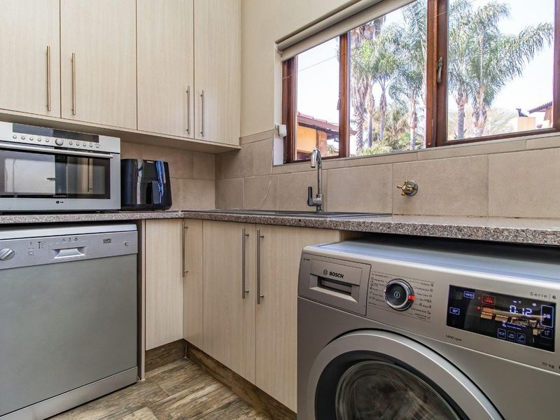 Functional scullery featuring light wood cabinetry, granite countertops, stainless steel sink, and dedicated space for a dishwasher and washing machine.