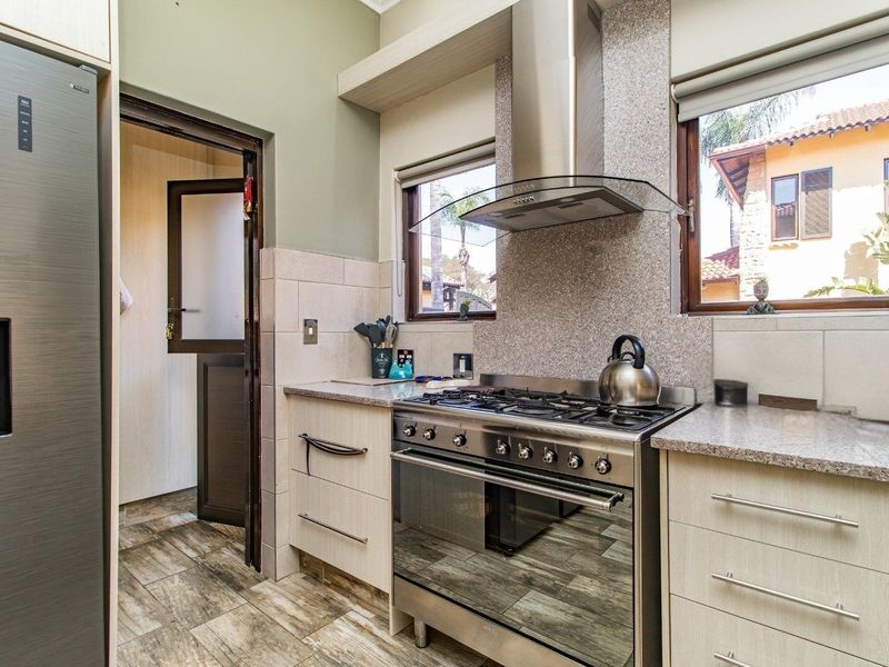 A well-maintained kitchen featuring granite countertops, a gas stove with an extractor fan, and modern cabinetry with tiled flooring.