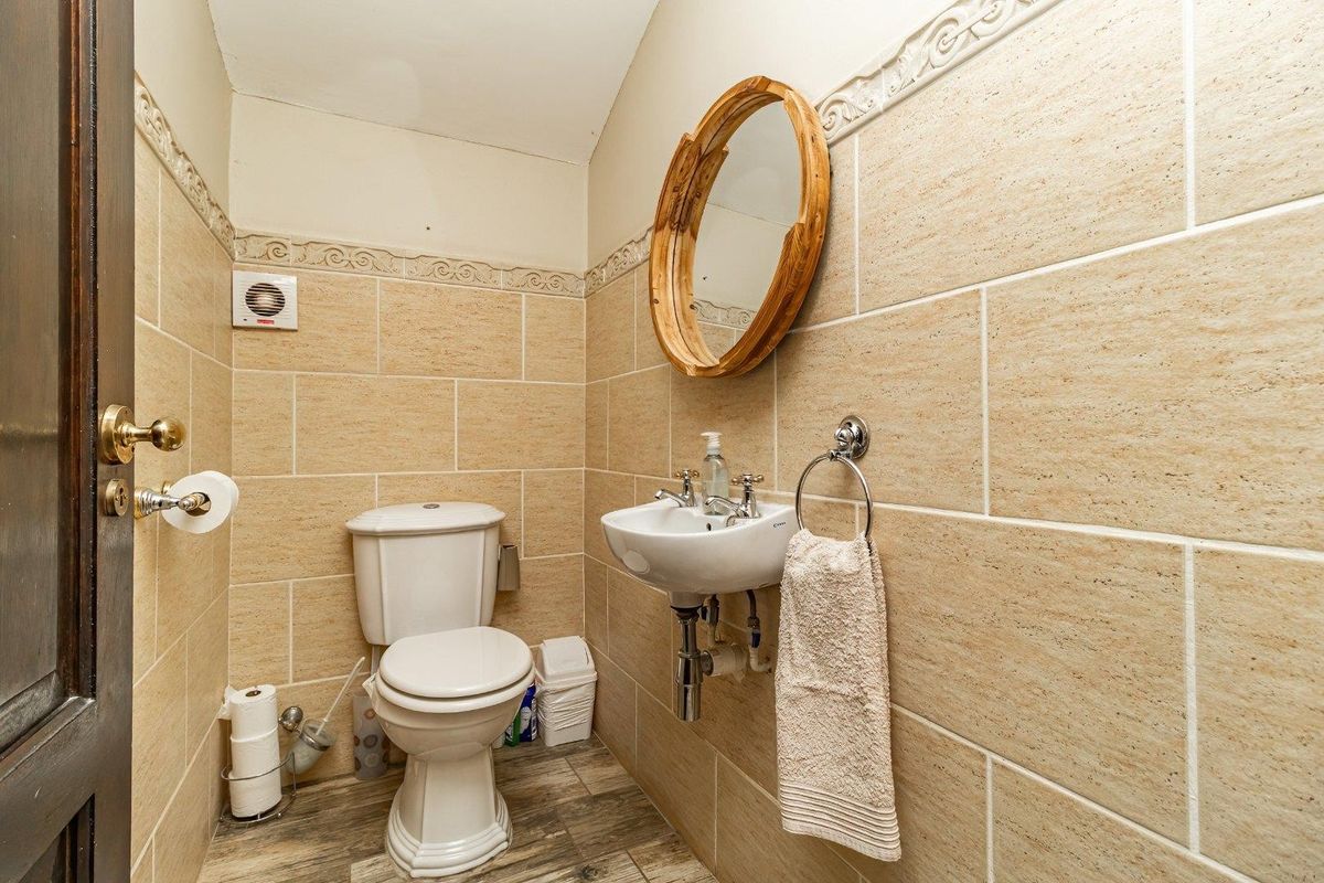 A compact bathroom featuring tiled walls, a wall-mounted basin, and a standard toilet, finished with neutral tones.