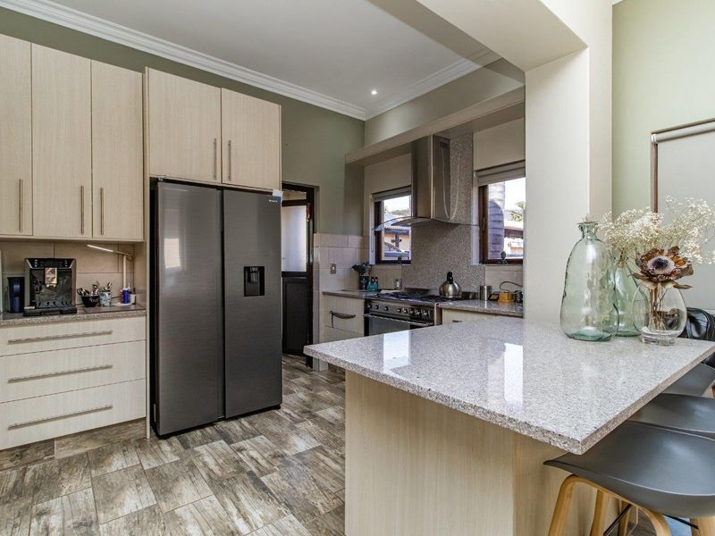 Modern kitchen featuring light wood cabinetry, granite countertops, a breakfast bar, and stainless steel appliances with tiled flooring.