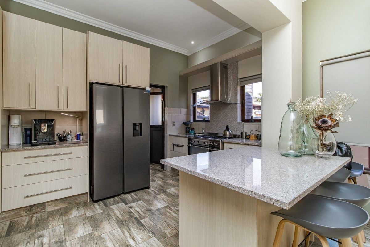 Modern kitchen featuring light wood cabinetry, granite countertops, a breakfast bar, and stainless steel appliances with tiled flooring.