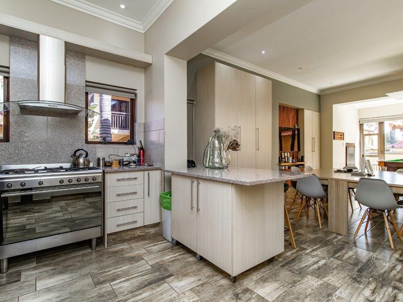 Spacious open-plan kitchen and dining area featuring modern cabinetry, granite countertops, a gas stove with extractor, and durable wood-look tiled flooring.