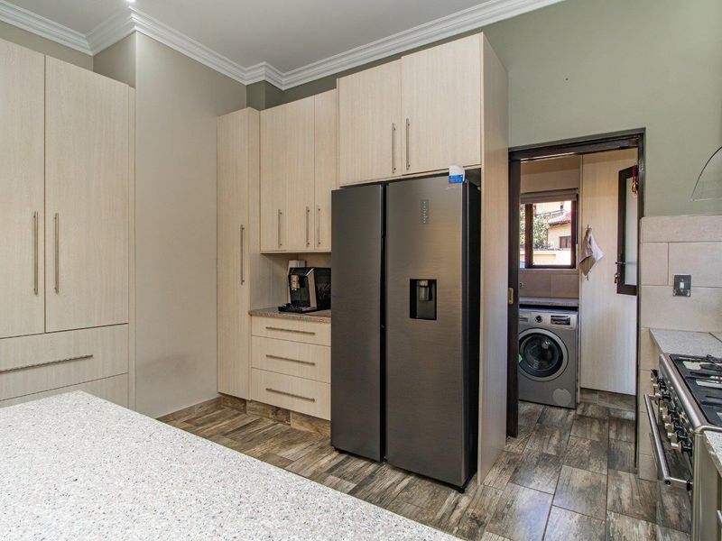 Modern kitchen featuring light wood cabinetry, stone countertops, gas hob, and extractor fan, with an adjacent scullery area visible.