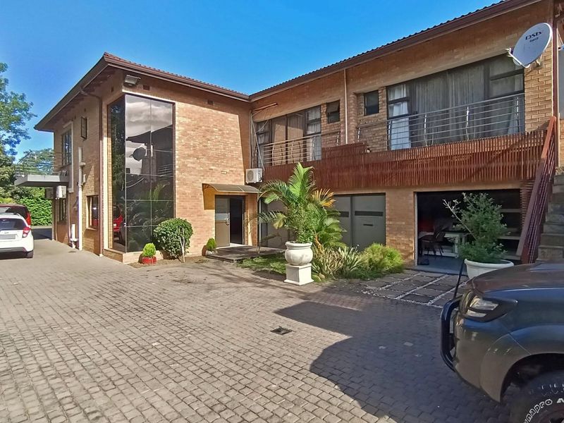 A multi-level brick residential property featuring a paved driveway, balcony with metal railings, and external access stairs.