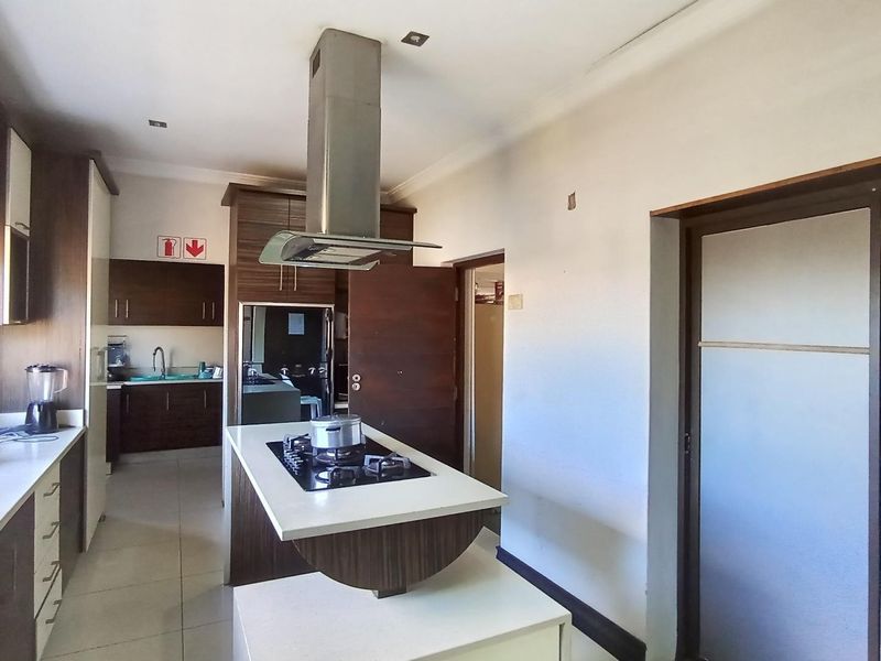 Modern kitchen featuring a central island with a gas hob, stainless steel extractor fan, ample built-in cabinetry, and tiled flooring.