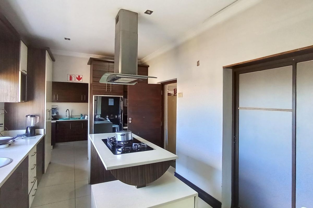 Modern kitchen featuring a central island with a gas hob, stainless steel extractor fan, ample built-in cabinetry, and tiled flooring.