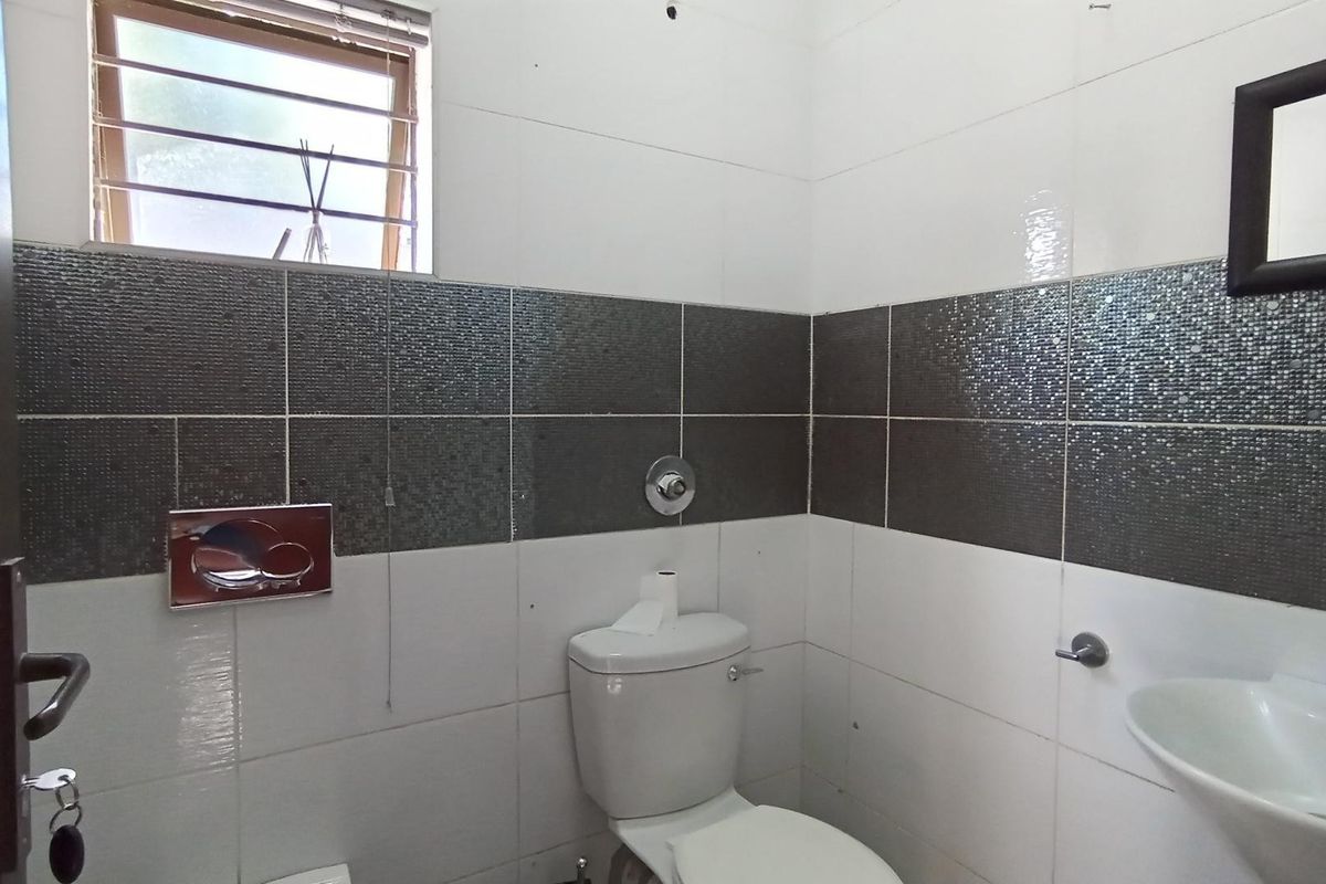 A clean, functional bathroom featuring a wall-mounted toilet, pedestal washbasin, and modern two-tone tiled walls with a window for natural light.