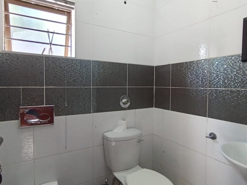 A clean, functional bathroom featuring a wall-mounted toilet, pedestal washbasin, and modern two-tone tiled walls with a window for natural light.