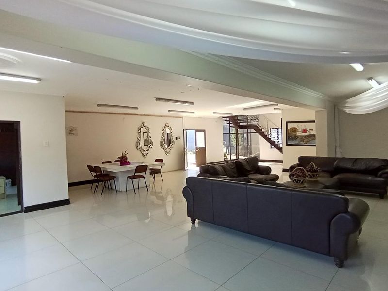 Spacious open-plan living and dining area featuring large format floor tiles, recessed lighting, and an integrated staircase leading to the upper level.