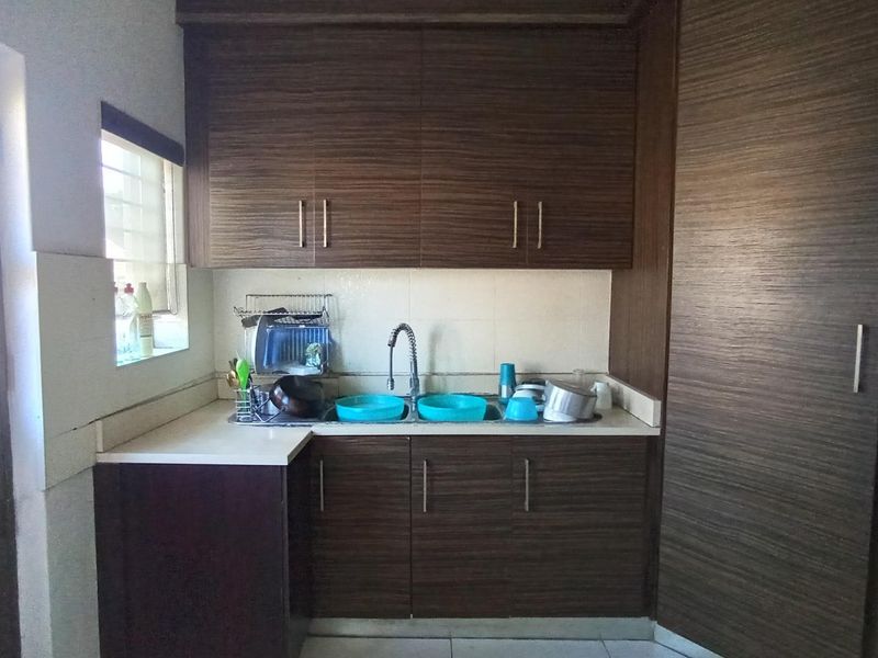A functional scullery area featuring dark wood-grain cabinetry, a stone countertop, and a stainless steel sink with a gooseneck faucet.