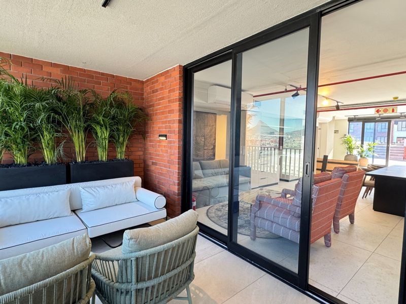 A modern covered balcony featuring exposed brick walls, large sliding glass doors, and tiled flooring, providing a seamless transition to the interior living space.