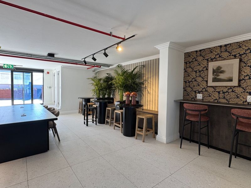 A modern open-plan communal area featuring tiled floors, exposed industrial-style fire piping, track lighting, and a built-in bar counter with seating.