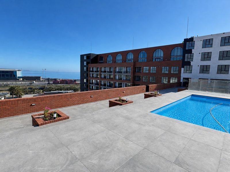 Rooftop pool area featuring a modern tiled deck, glass balustrades, and built-in brick planters with panoramic views of the harbor and city.