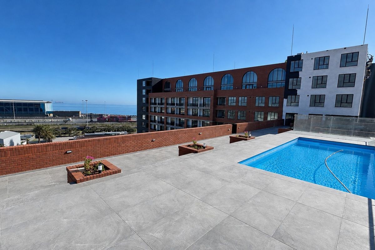 Rooftop pool area featuring a modern tiled deck, glass balustrades, and built-in brick planters with panoramic views of the harbor and city.