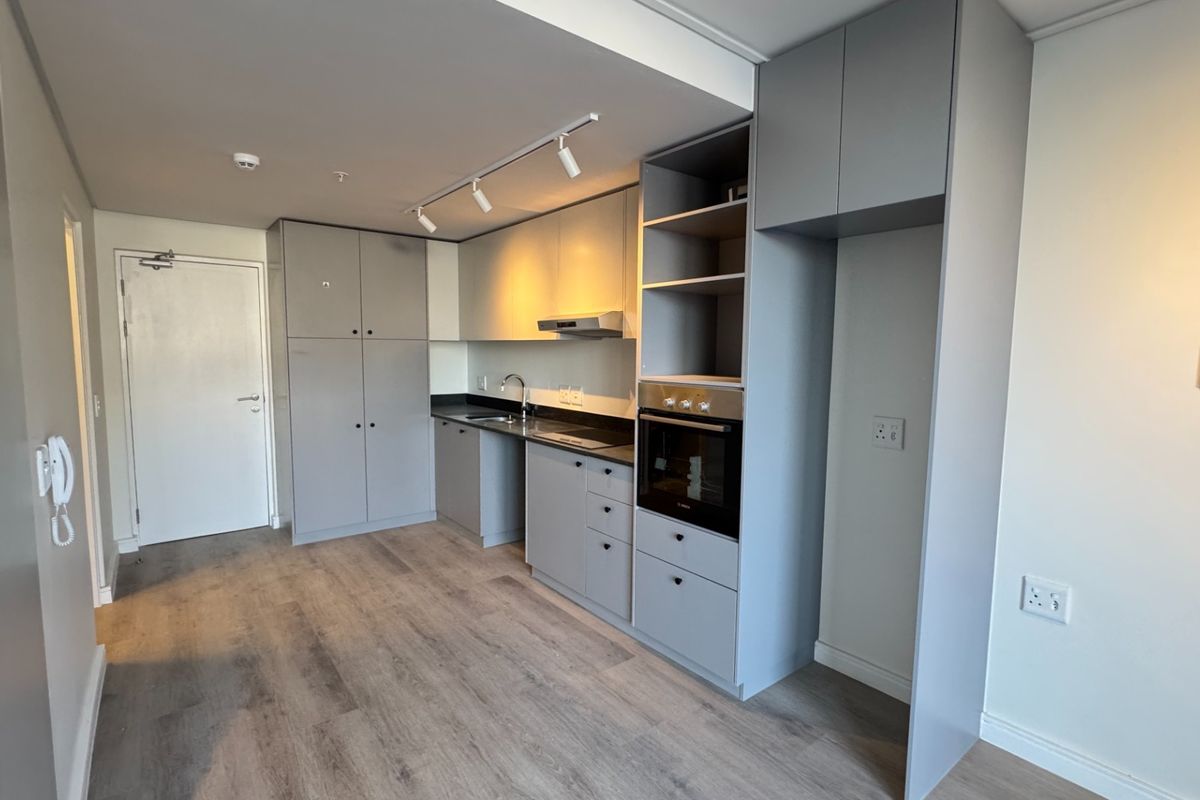 Modern, compact kitchen featuring sleek grey cabinetry, integrated oven, extractor fan, and durable laminate flooring in an open-plan layout.