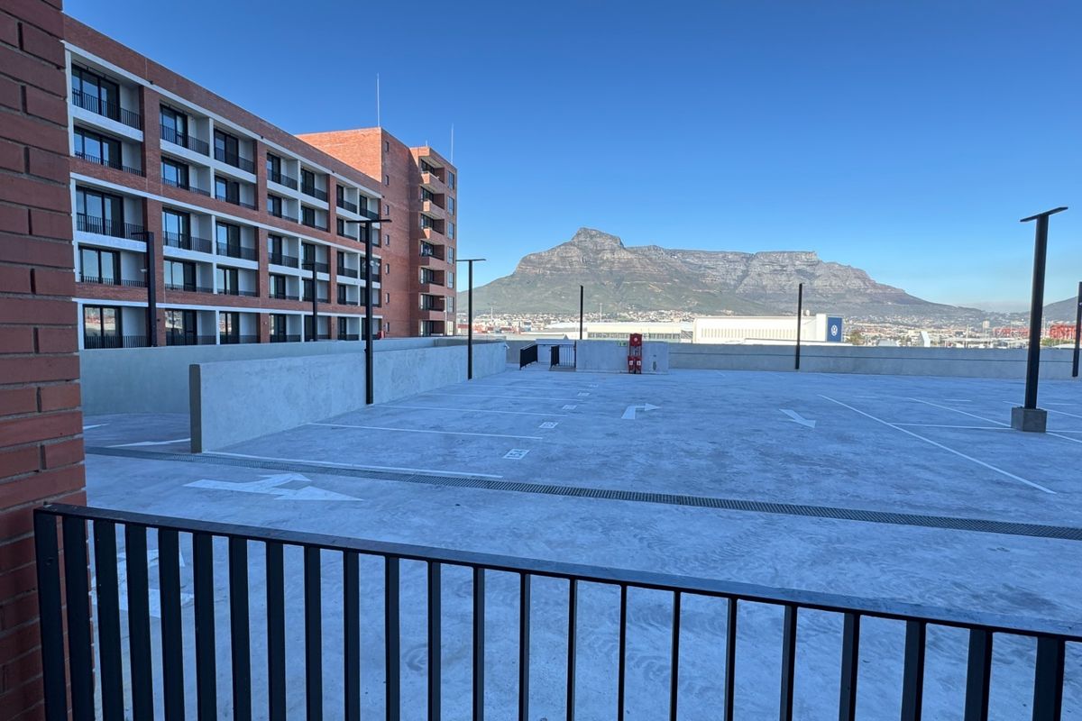 An open-air parking area featuring a concrete surface, brick building facade, and clear views of the mountain landscape.