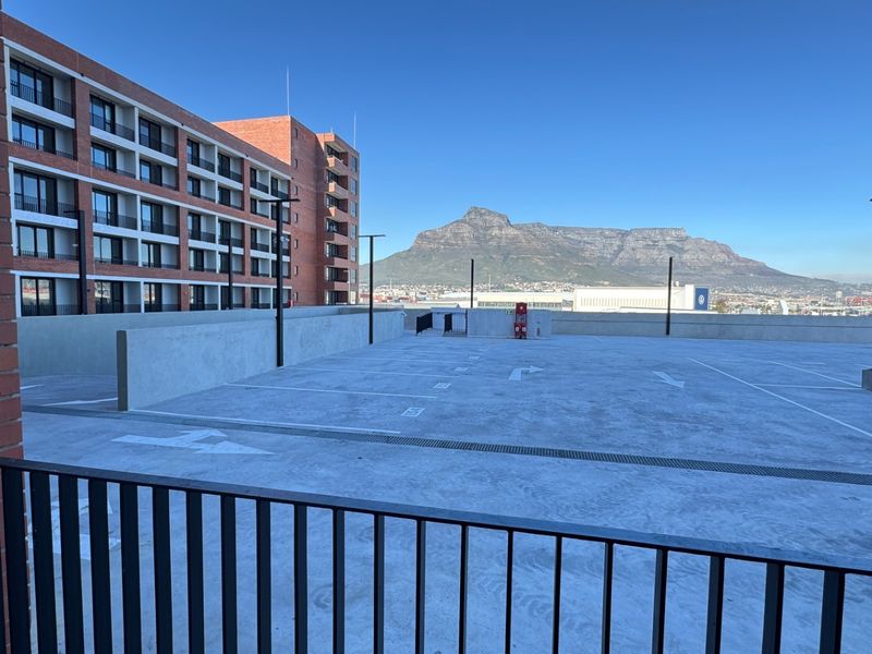 An open-air parking area featuring a concrete surface, brick building facade, and clear views of the mountain landscape.