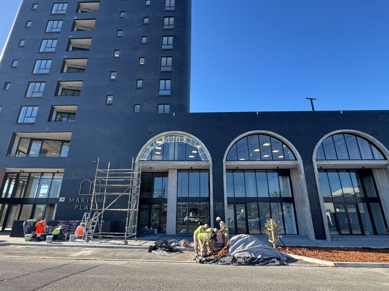 Modern high-rise apartment building exterior featuring dark brickwork, prominent arched windows, and ground-level commercial storefronts currently under final construction.