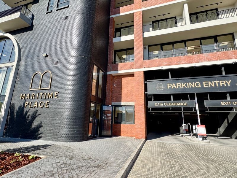 Front exterior view of Maritime Place apartment building, featuring a modern brick facade, secure parking garage entrance, and balconies.