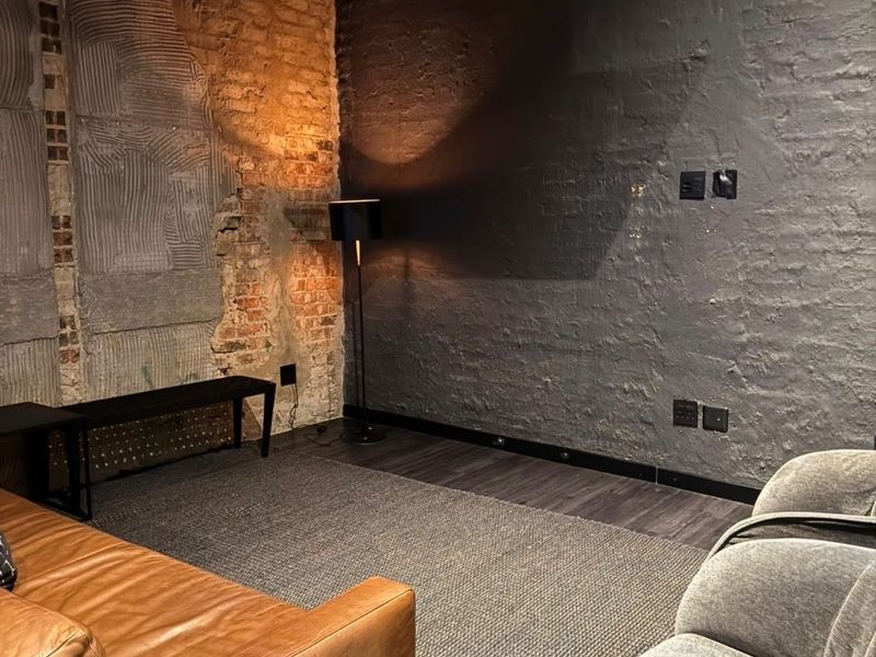 Industrial-style living area featuring exposed brickwork, raw ceiling pipes, and dark painted masonry walls, creating a modern urban aesthetic.