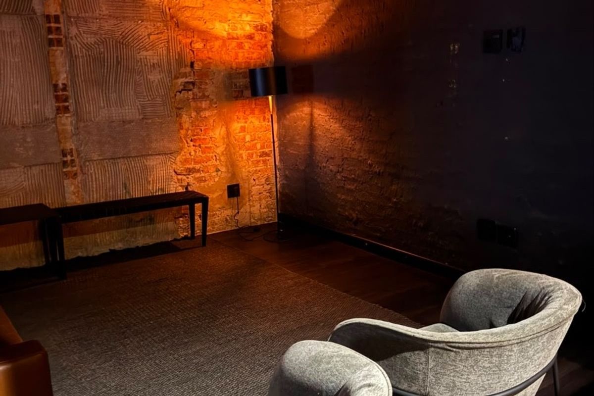 A living area featuring exposed brick walls and dark hardwood flooring, currently presented with an industrial, unfinished aesthetic.