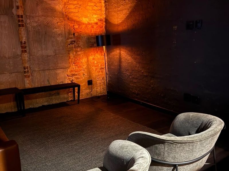 A living area featuring exposed brick walls and dark hardwood flooring, currently presented with an industrial, unfinished aesthetic.