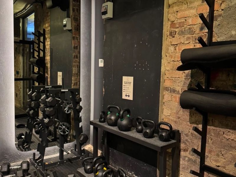 A compact gym space featuring exposed brick walls, durable rubber flooring, and integrated wall-mounted storage for fitness equipment.