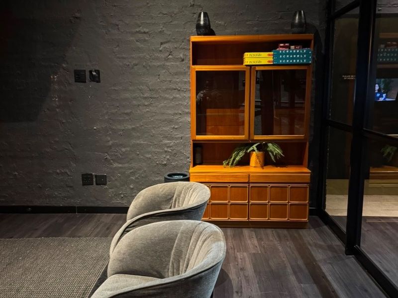 A modern living area featuring dark exposed brick walls, dark laminate flooring, and a sleek black metal-framed glass partition.