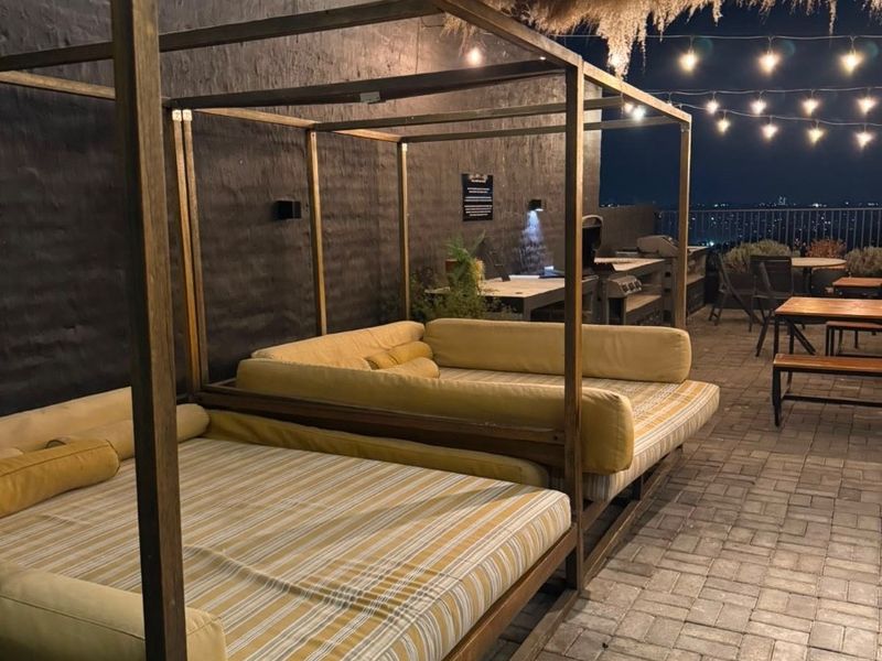 A covered outdoor patio area featuring paved flooring, built-in outdoor kitchen facilities, and ambient string lighting, overlooking a city view.