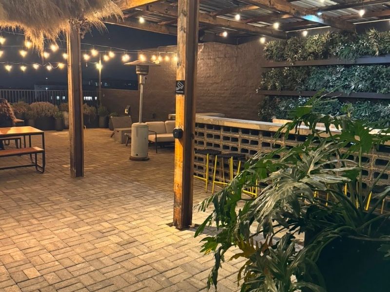 A well-appointed covered patio featuring a timber pergola, brick-paved flooring, a built-in brick bar, and a vertical garden wall with ambient string lighting.