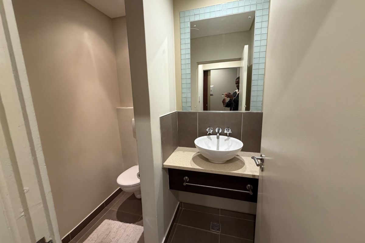 A modern guest bathroom featuring a vessel sink on a stone vanity, wall-mounted toilet, and neutral tiled flooring.
