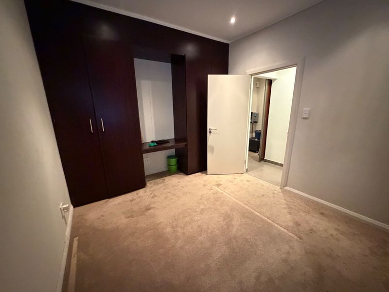 An empty bedroom featuring dark wood built-in cupboards with an integrated desk area, recessed lighting, and carpeted flooring.