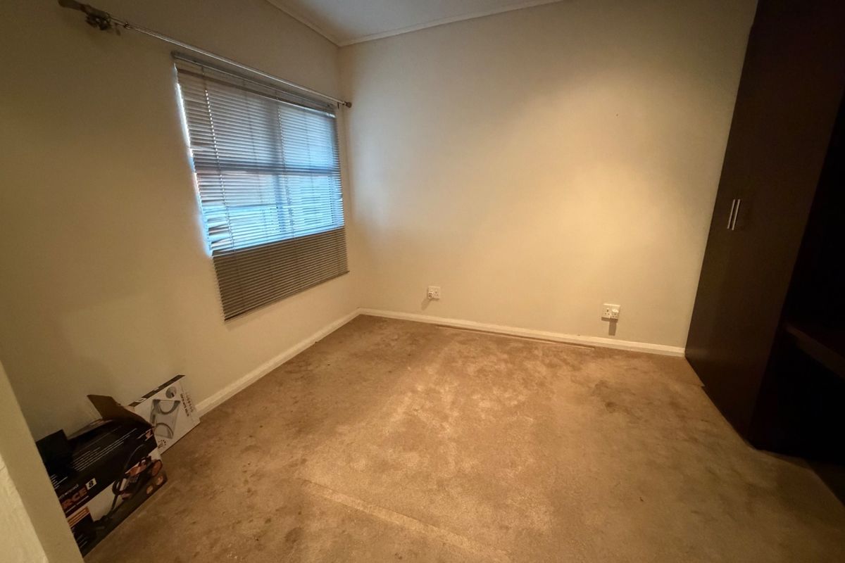 An empty bedroom featuring built-in wardrobe storage, venetian blinds, and carpet flooring. The room requires cosmetic updates to the flooring.