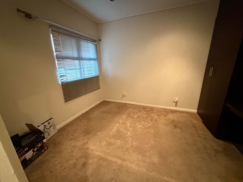 An empty bedroom featuring built-in wardrobe storage, venetian blinds, and carpet flooring. The room requires cosmetic updates to the flooring.