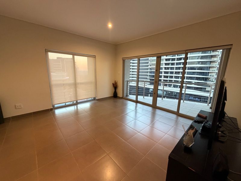 Spacious, light-filled living area featuring neutral tiled flooring, large sliding glass doors leading to a balcony, and modern roller blinds.