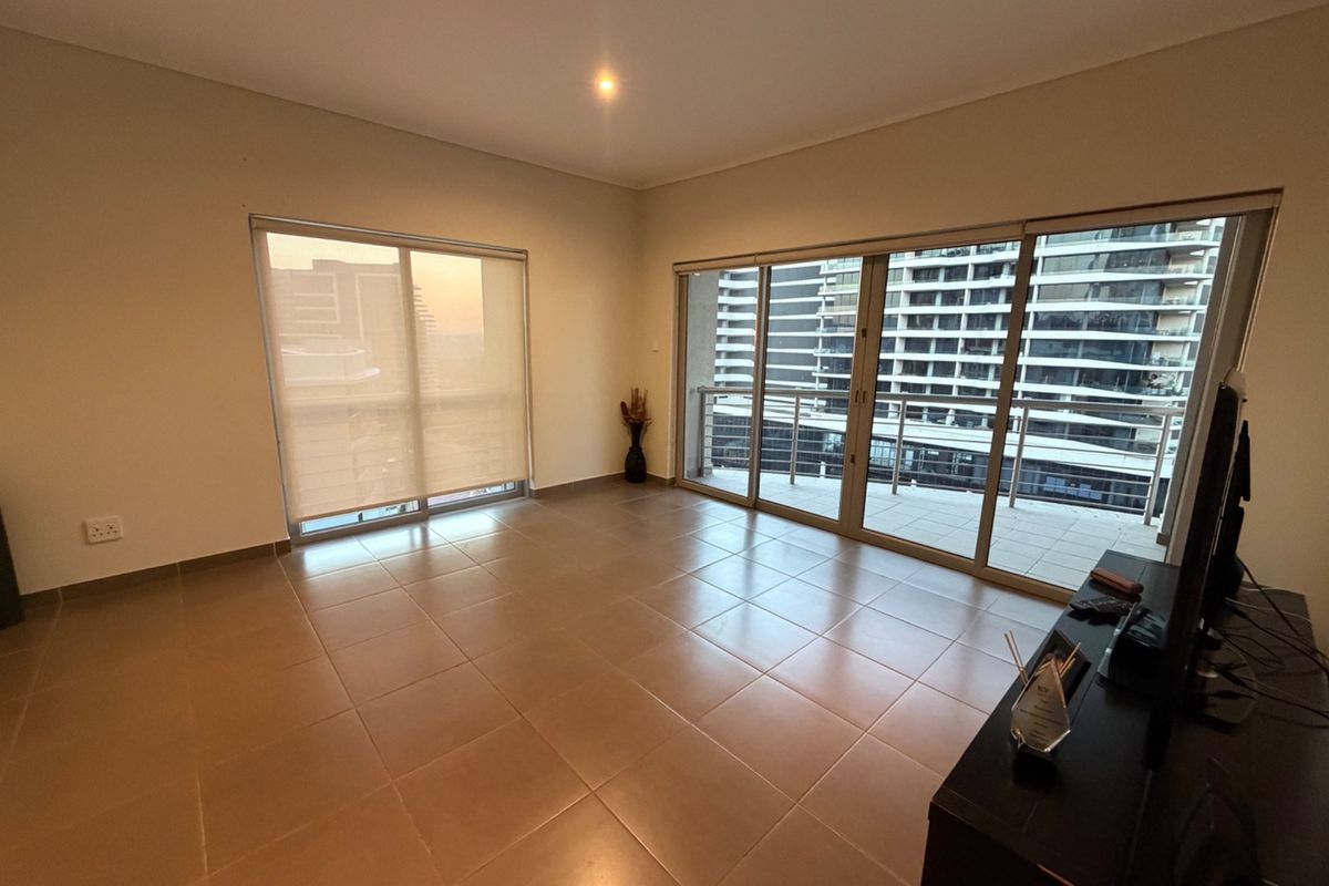 Spacious, light-filled living area featuring neutral tiled flooring, large sliding glass doors leading to a balcony, and modern roller blinds.