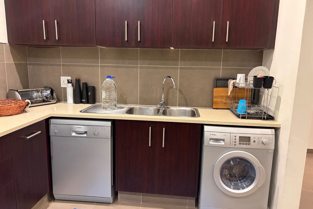 A functional kitchen area featuring dark wood cabinetry, stone countertops, a double stainless steel sink, and integrated laundry and dishwashing appliances.