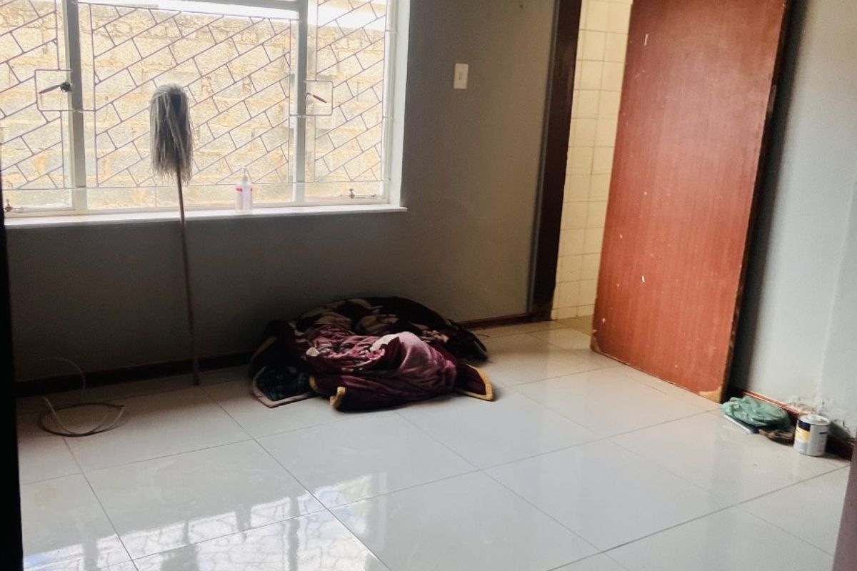 A vacant bedroom featuring large white floor tiles, a sliding door, and a window fitted with security bars.