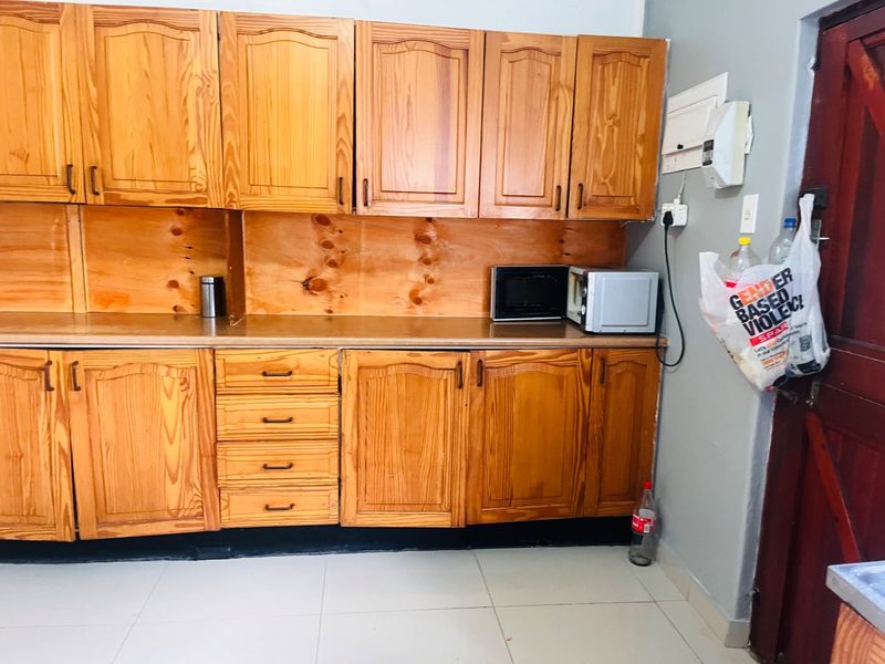 A functional kitchen featuring wooden cabinetry, laminate countertops, and tiled flooring, providing ample storage and workspace.