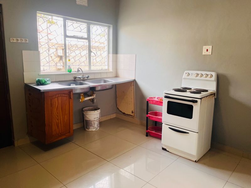 A functional kitchen featuring tiled flooring, a double sink with tiled splashback, and a freestanding stove, requiring some cabinetry repairs.