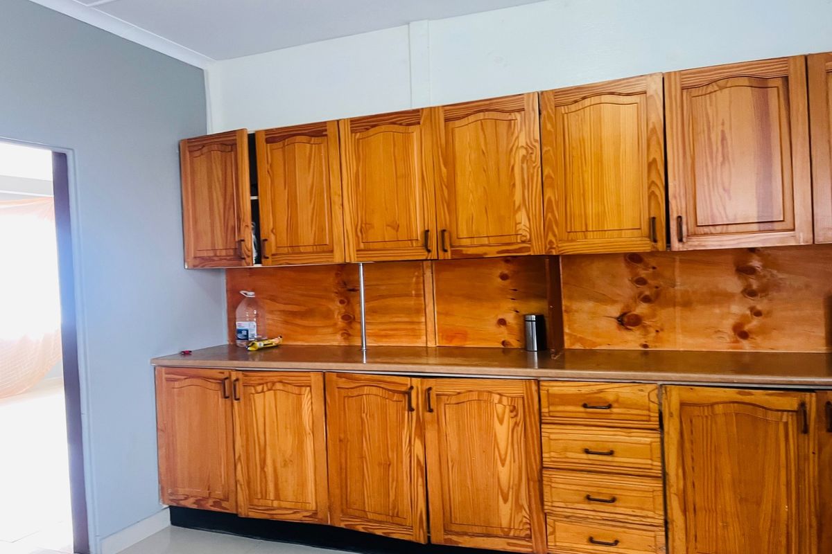 A functional kitchen area featuring extensive wooden cabinetry, a laminate countertop, and tiled flooring, offering a classic aesthetic ready for modern updates.