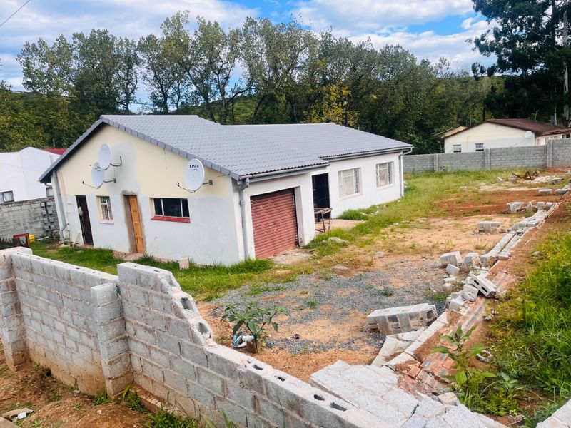 Rear view of a single-story house featuring a tiled roof, roller garage door, and an unfinished concrete block boundary wall in the yard.