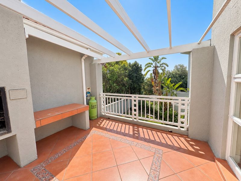 A spacious covered balcony featuring a built-in braai, tiled prep area, and a pergola, offering an ideal space for outdoor entertaining.